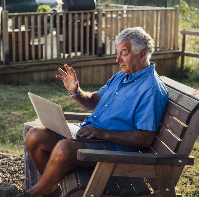 Man in blue shirt and shorts sitting outdoors on his laptop.