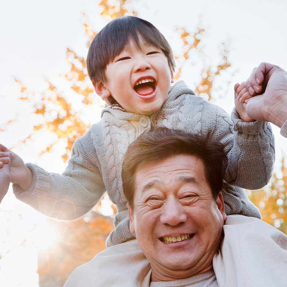 Happy elderly man holds happy child above his shoulders.